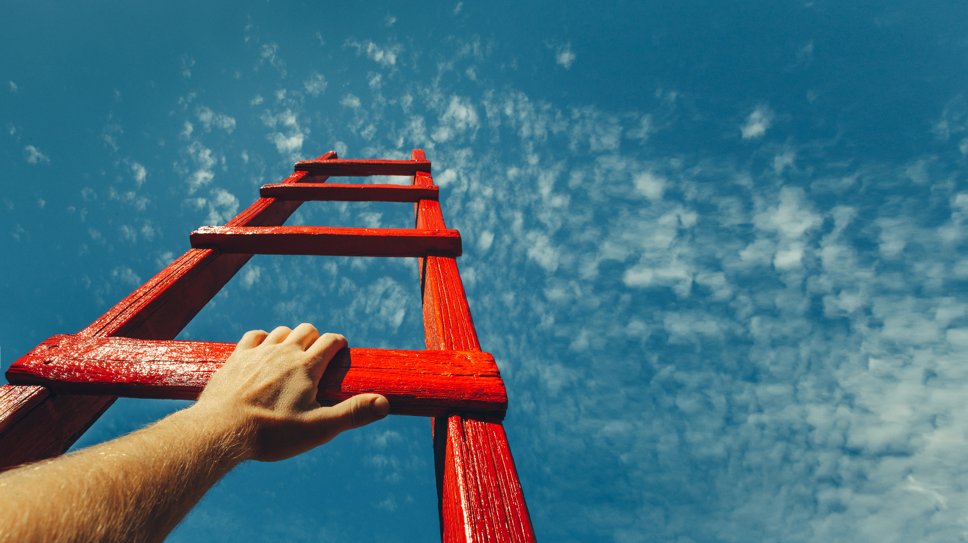 A hand reaching for the next rung of a red ladder against an open sky